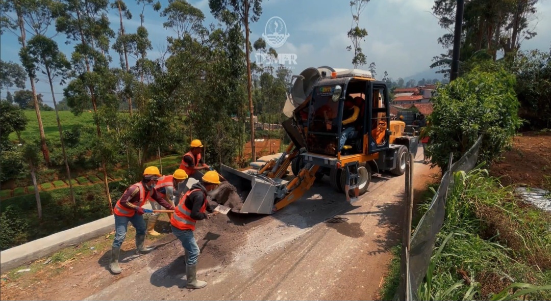 Pekerja bersama armada mobile batching plant atau self loading concrete mixer milik Dinas Bina Marga dan Penataan Ruang Jawa Barat saat melakukan proses pemuatan material untuk pembangunan jalan di kawasan pedesaan.